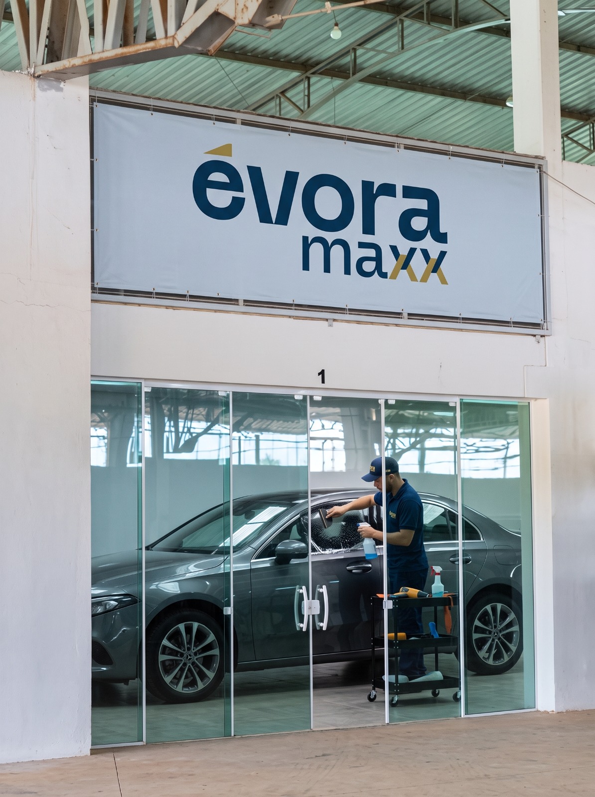 Banner Évora Maxx sobre a sala de aplicação com técnico aplicando película em sedã